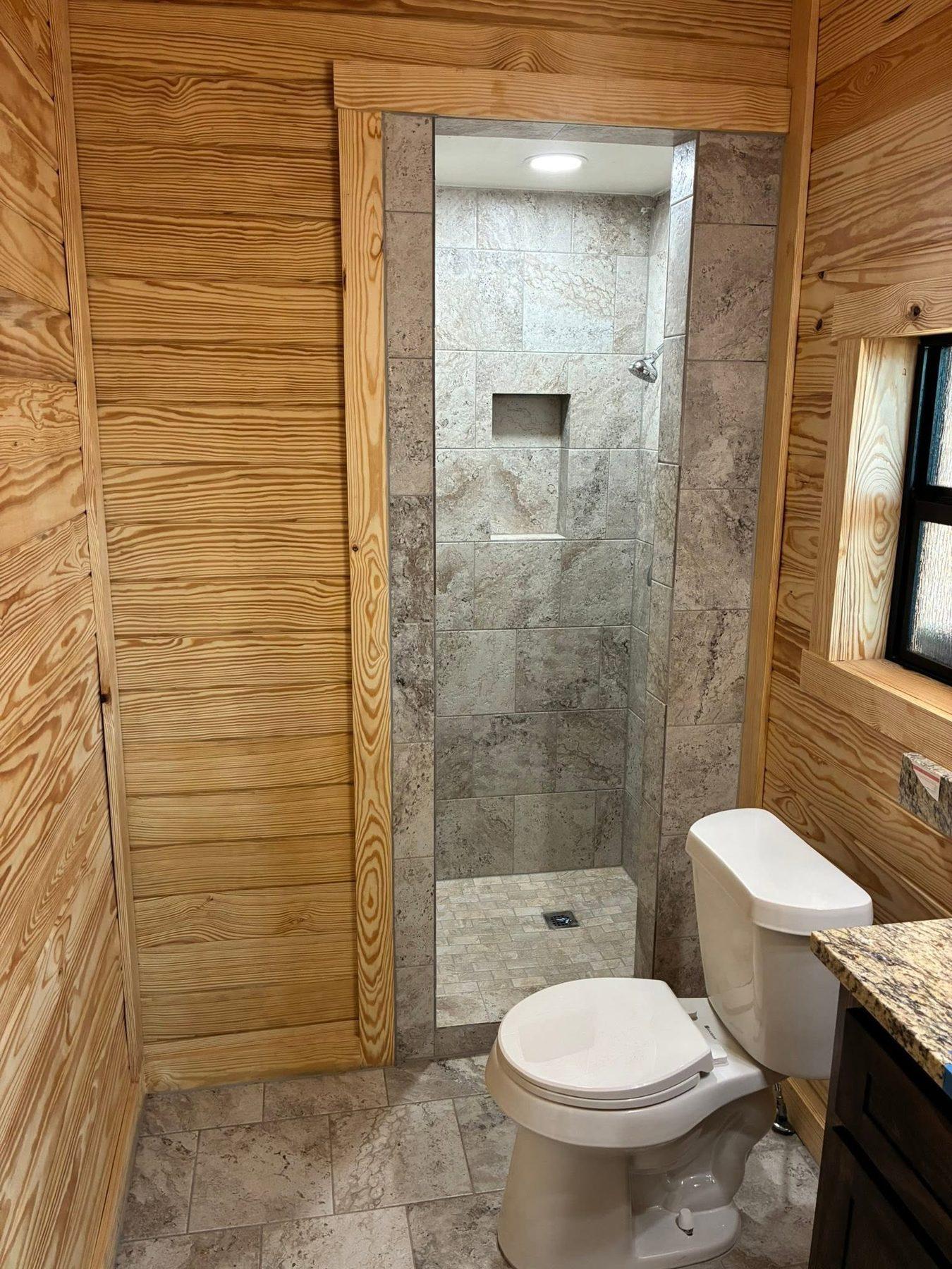 Tiled walk-in shower set into a pine-panelled bathroom