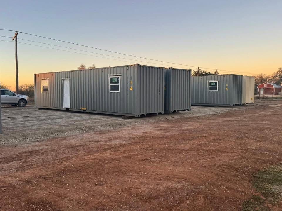 Two shipping-container workforce housing units on a graded gravel pad at sunset, West Texas