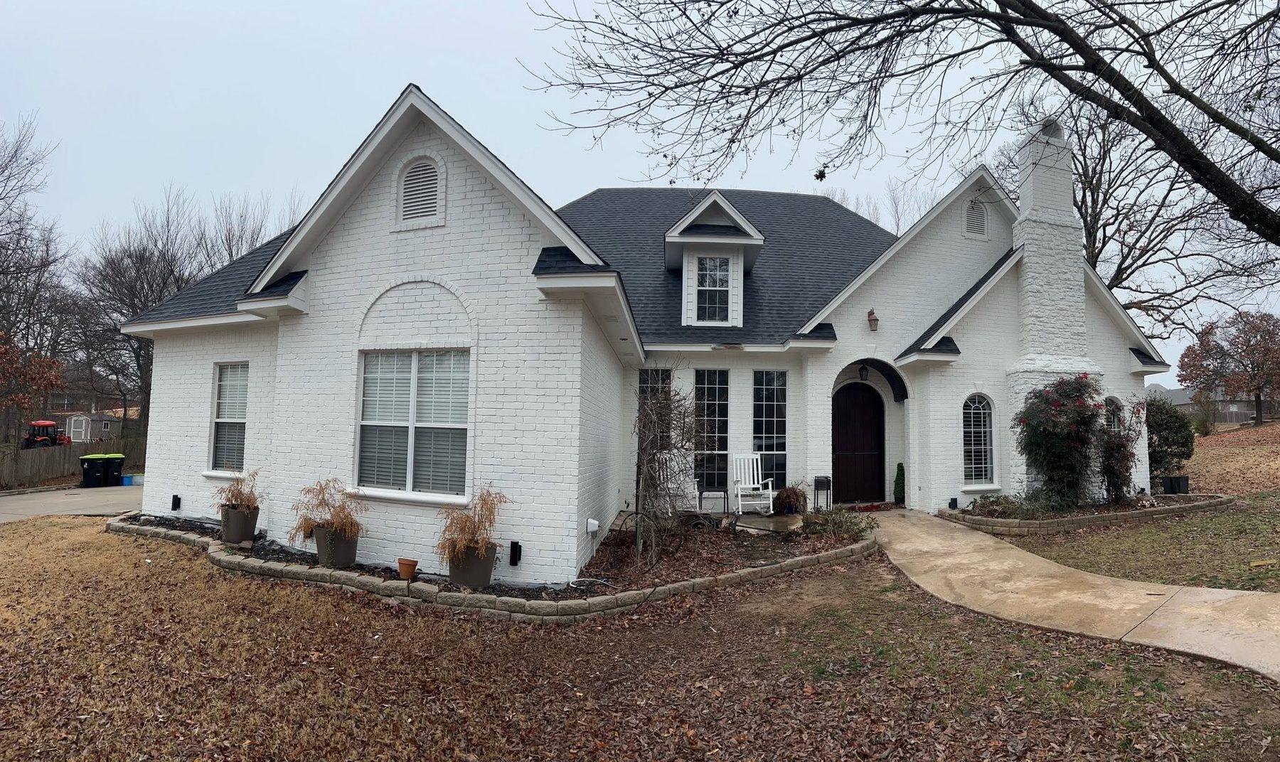 A completed white brick home with a dark shingle roof
