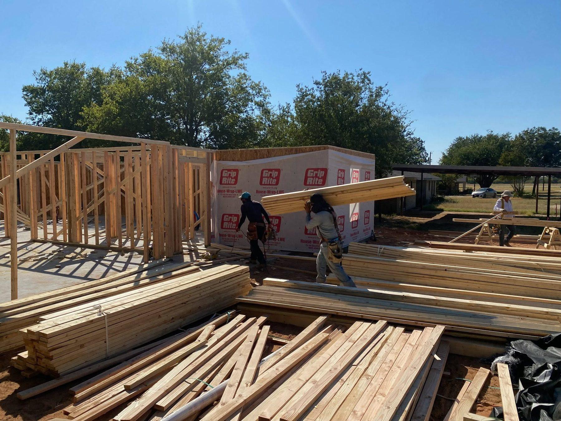 Crew setting wall framing on a new home under a blue sky